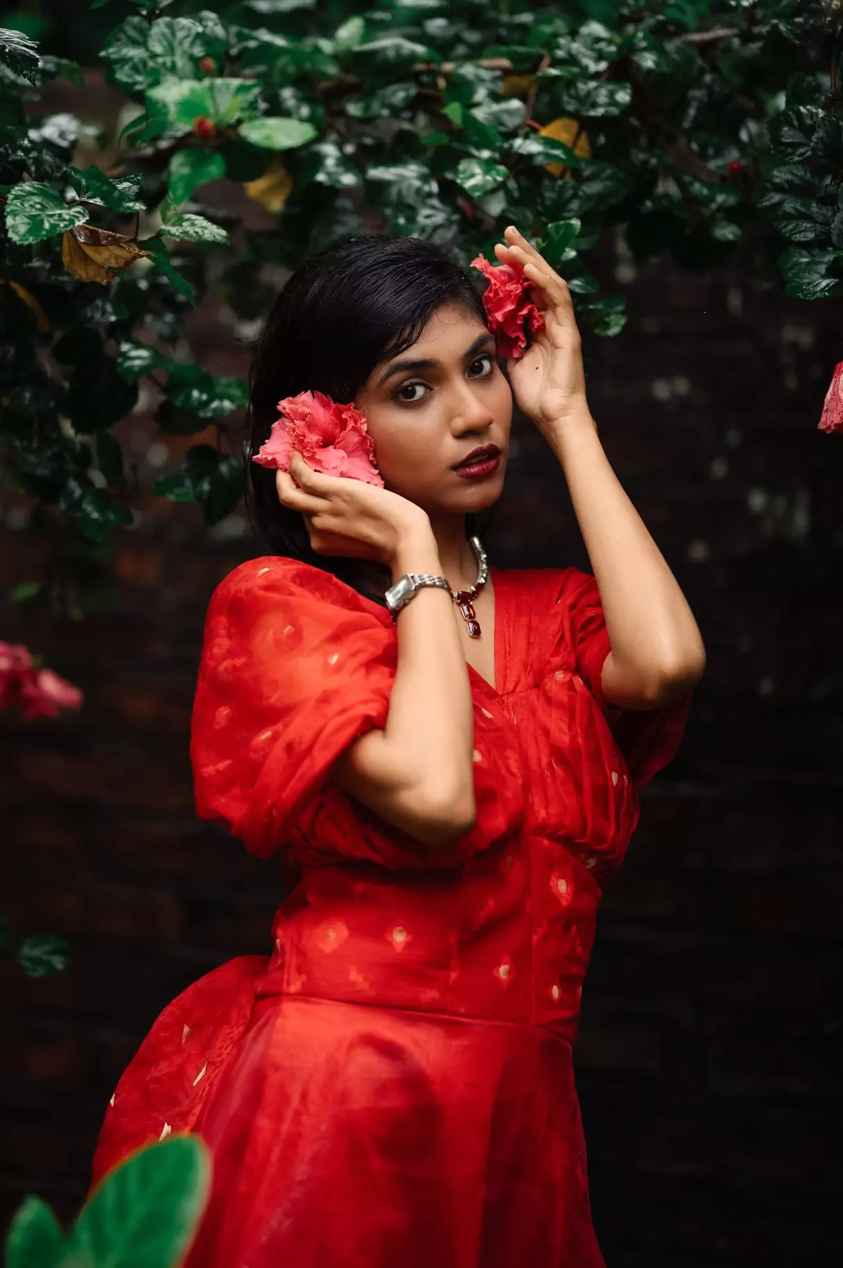Red dress style photo, flower in hand, standing by lush green foliage