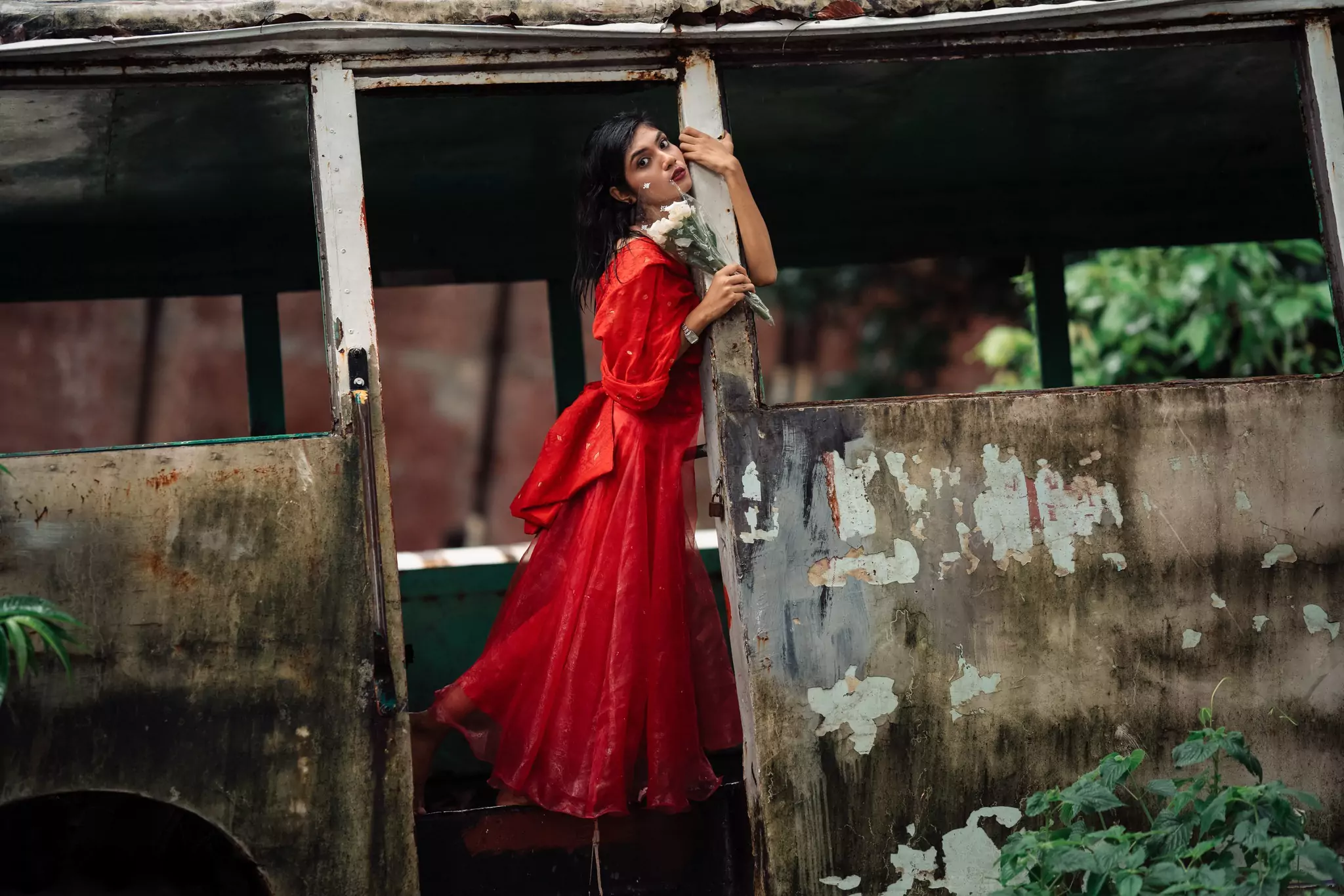 Woman in flowing red dress posing artistically beside a rustic shed outdoors