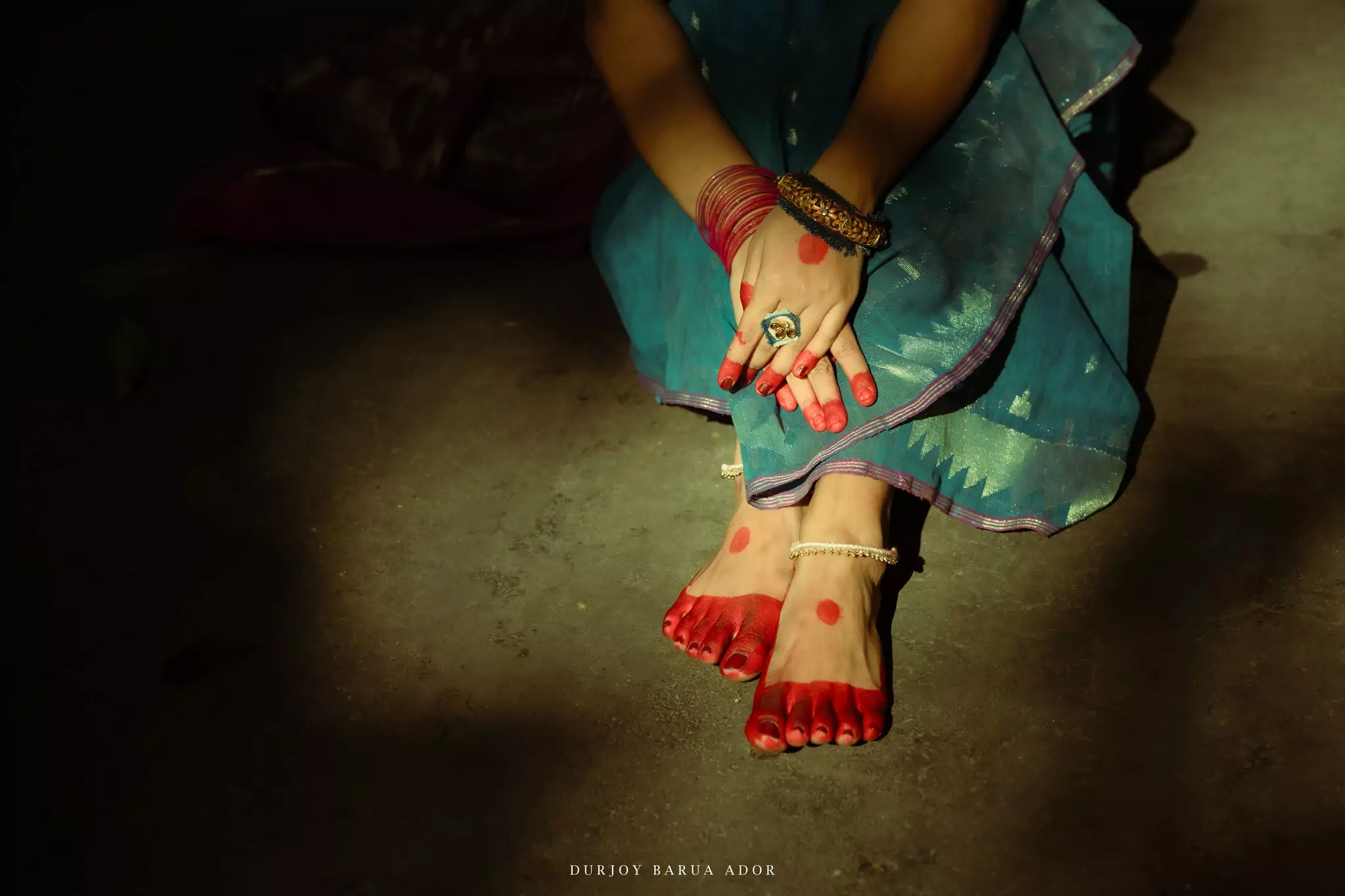 Traditional pose of crossed feet with alta and anklets in shadowed lighting.