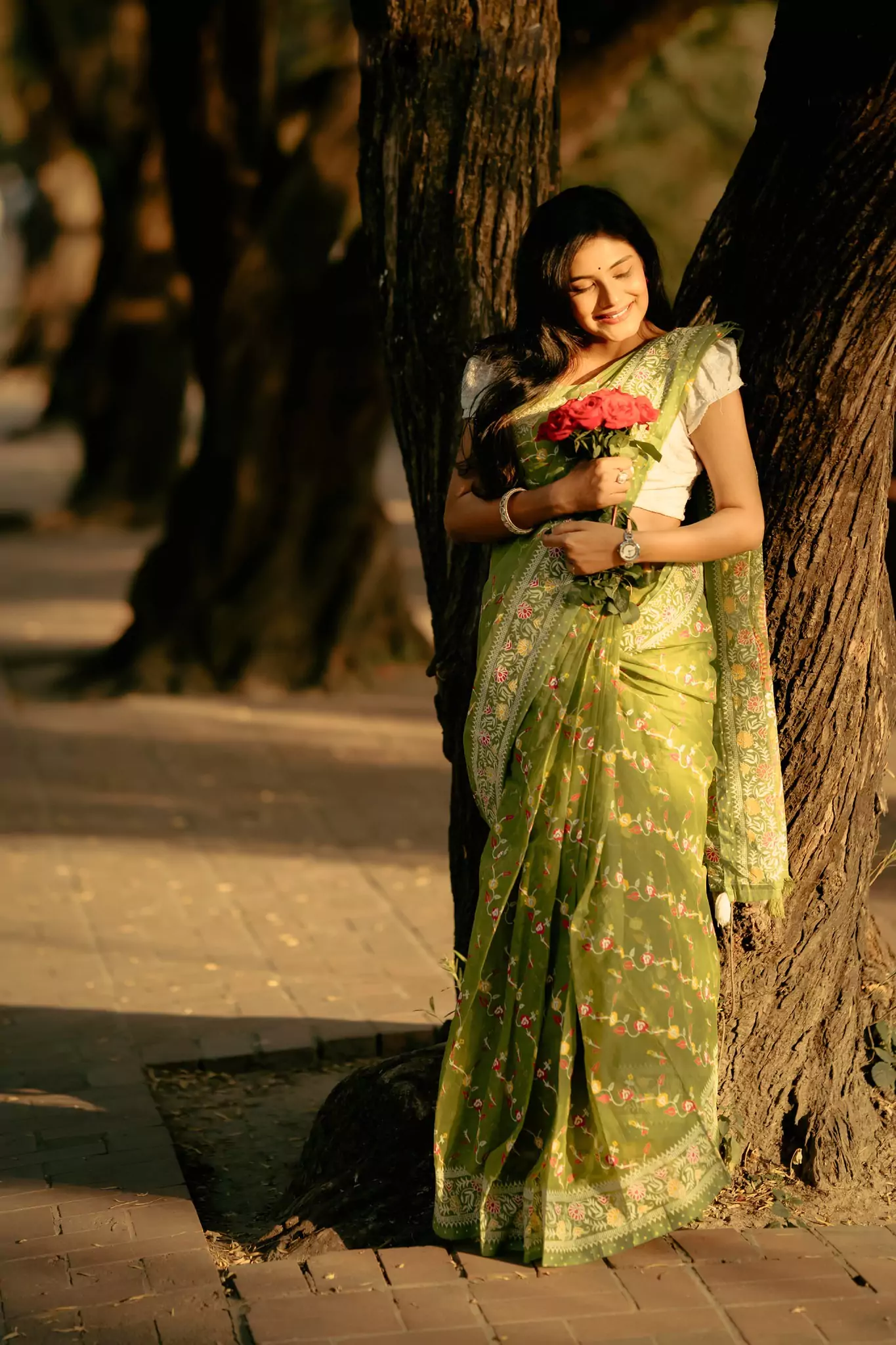 Woman in green saree holding bouquet, woodland sunlight setting