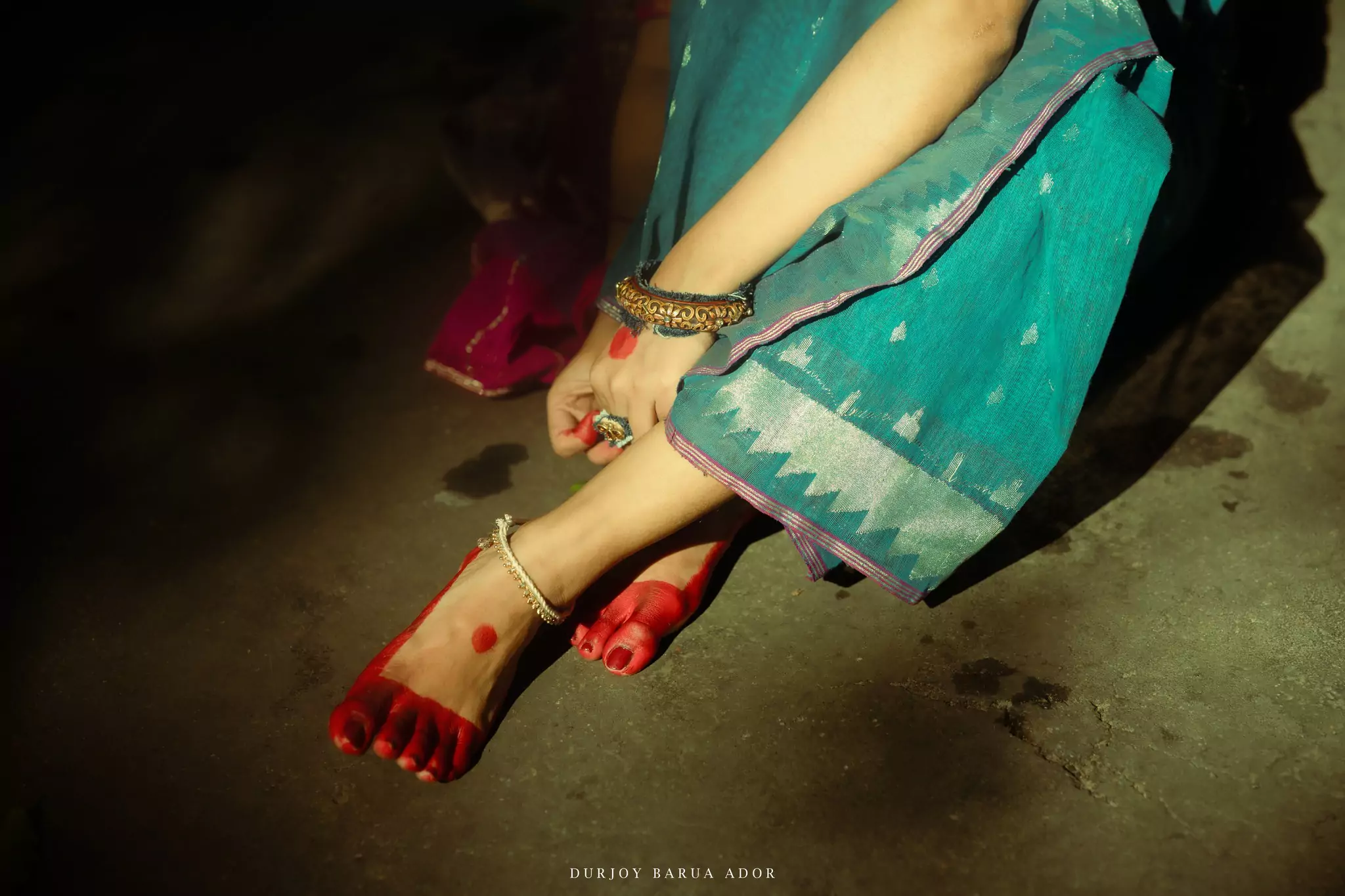 Feet of a woman decorated with alta, wearing traditional anklets, captured in warm light.