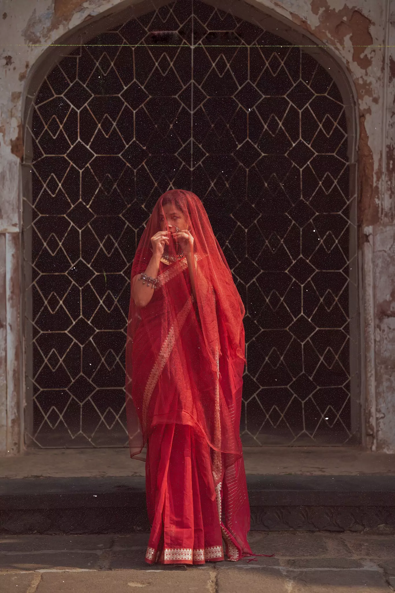 Traditional Indian woman in red saree standing in front of an ancient arched doorway